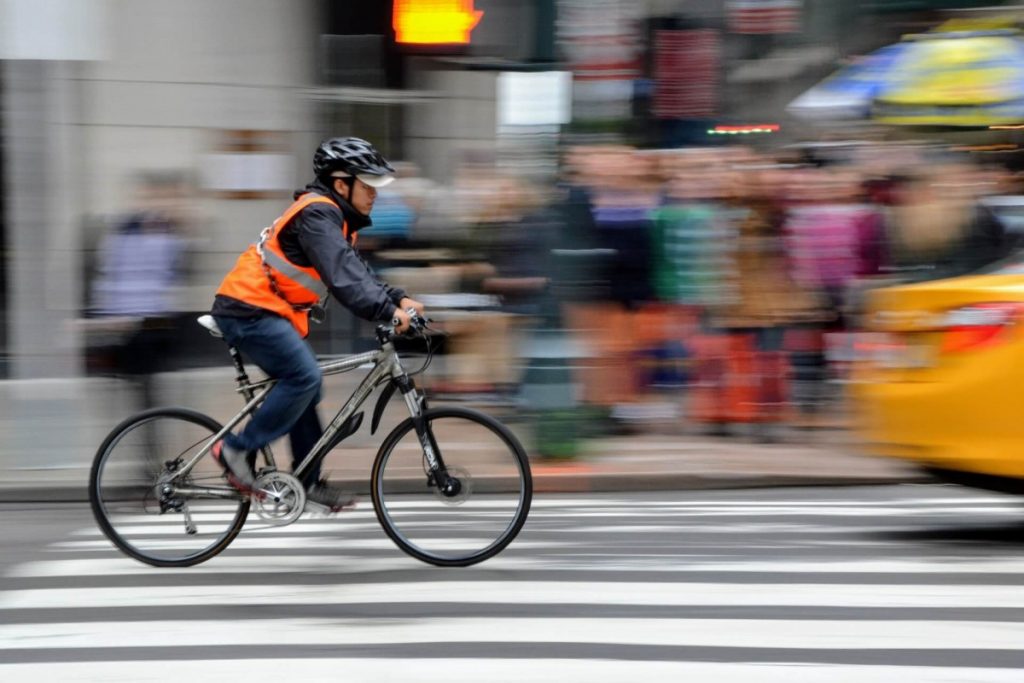 Man riding an orange safety vest riding a bicycle